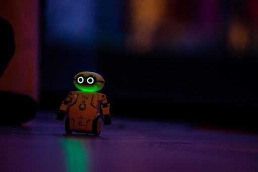 Small robot with glowing green eyes and wheels moving through a dark room